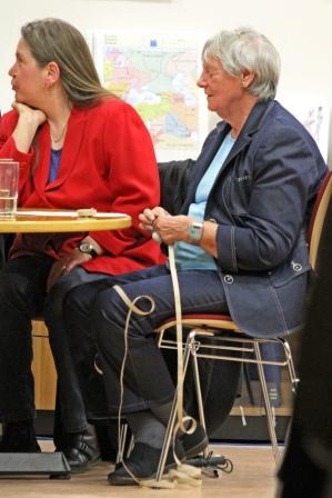 Auf dem Bildausschnitt sieht man Frau Heike Herrmann-Hofstetter
  und Frau Ruth Wunsch w�hrend der Lesung des Buches �Blinde-Sch�nheit�
  auf der Leipziger Buchmesse 2010. Die beiden Damen sitzen
  nebeneinander an einem Tisch.
  Frau Wunsch, deren K�rper nach links ausgerichtet ist, sitzt auf
  einem Stuhl am rechten Tischende, sodass der Betrachter sie von der
  Seite sehen kann. Sie ist eine flotte �ltere Dame mit wei�em
  Kurzhaarschnitt. Sie tr�gt einen dunkelblauen Jeansanzug, aus der
  Jacke schimmert ein hellblaues T-Shirt. L�ssig sitzt sie mit
  �berkreuzten F��en da. Sie wirkt sehr konzentriert, denn sie wartet
  gerade auf ihren Einsatz als Vortragende.
  Noch lauscht Frau Herrmann aber ganz entspannt ihrer anderen Sitznachbarin, die
  mittig am Tisch sitzt, hier im Bildausschnitt aber nicht zu sehen
  ist. Sie wendet dieser ihren Kopf zu. Ihr langes mittelblondes Haar
  hat sie hinter die Ohren geklemmt, sodass es sanft auf ihren R�cken
  flie�t. Bekleidet ist sie mit dunkler Jeans und einem eleganten
  roten Jackett, aus dem ein gl�nzend blaues Seidenhemd hervorlugt.
  Zur gleichen Zeit ist Frau Wunsch vollkommen auf sich konzentriert.
  Offensichtlich macht sie sich bereit f�r ihre Lesung. So h�lt sie
  schon den Anfang des Textstreifens mit Brailleschrift (der
  Punktschrift, mit deren Hilfe sie Texte mit dem Tastsinn ihrer Finger
  erlesen kann) in den H�nden. Sehr sensibel ertastet sie mit den
  Fingerkuppen der rechten Hand bereits die ersten W�rter. Der
  lange Papierstreifen f�llt wie eine Girlande locker auf den Boden, wo
  das Papier sich in Ringen sammelt, w�hrend das Ende der Papierschlange
  leicht gekr�uselt �ber ihrem linken Bein liegt. Gleich beginnt ihr
  Vortrag und dann wird Frau Wunsch die lange Papierschlange sanft
  abtastend durch ihre H�nde gleiten lassen und ihren pers�nlichen Text
  zum Thema Sch�nheit dem interessierten Publikum vorlesen.